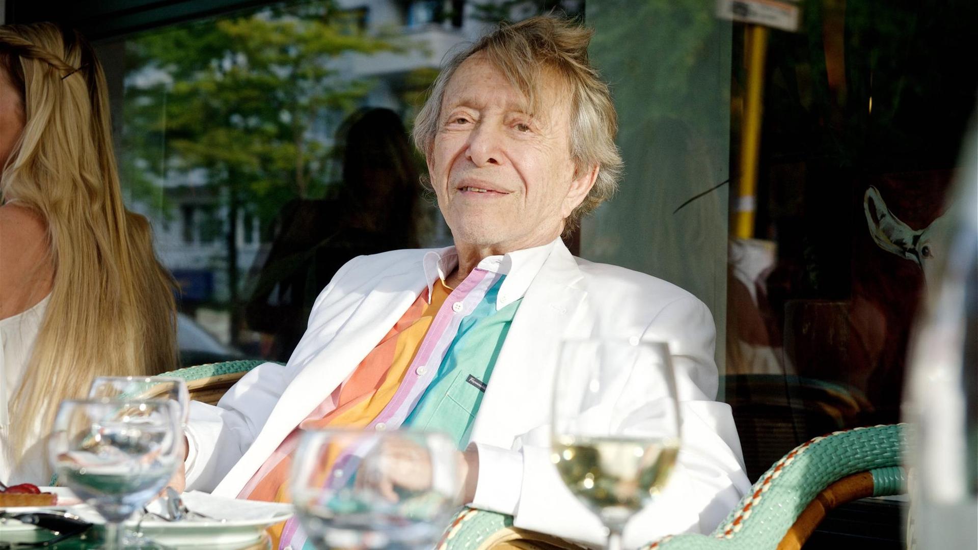 Rolf Eden sitzt an einem Caféhaustisch vor der Paris Bar in Berlin und isst Mittag.