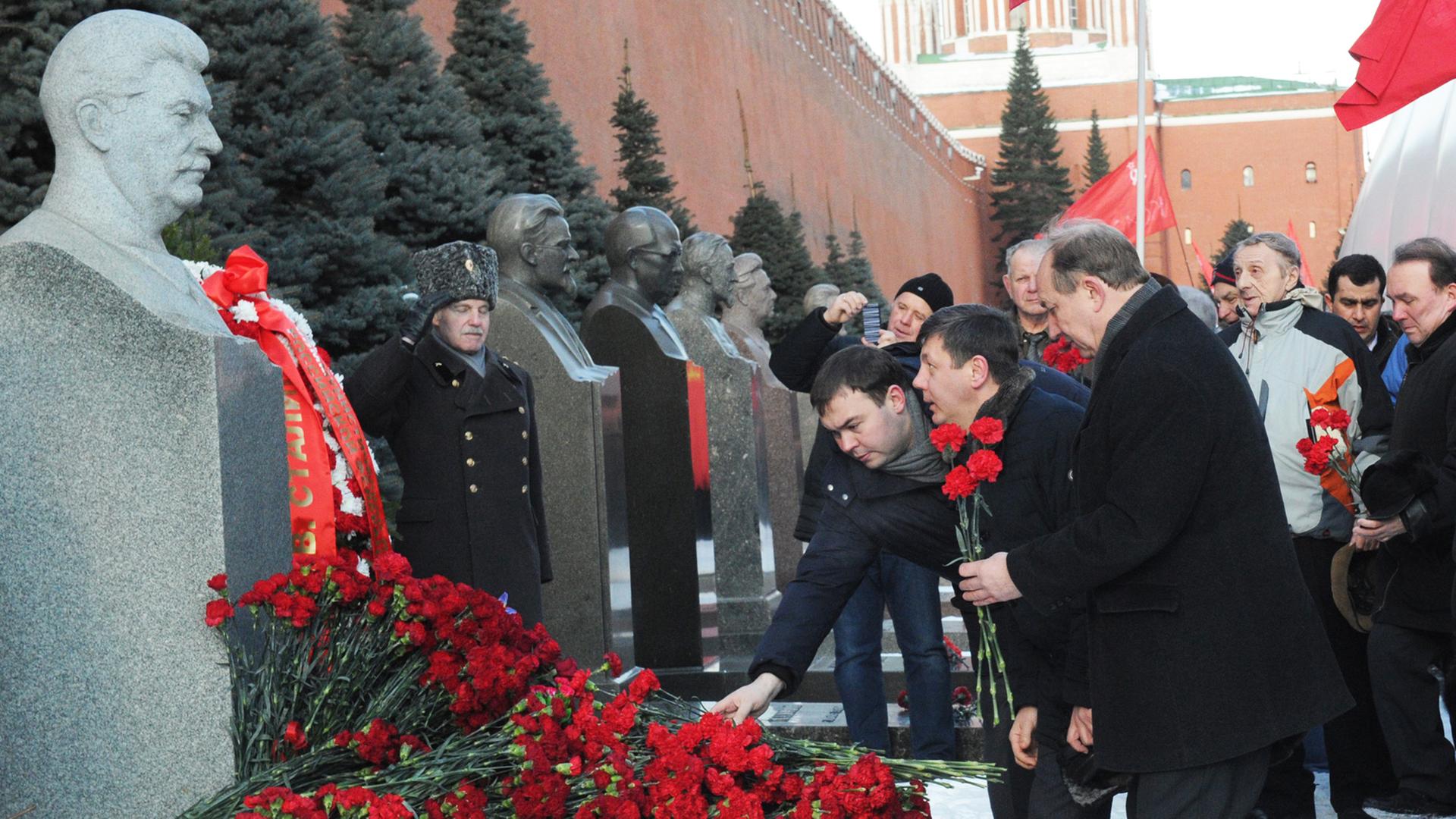 Politiker legen an einer Stalin-Büste Blumen nieder.