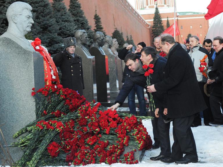 Politiker legen an einer Stalin-Büste Blumen nieder.
