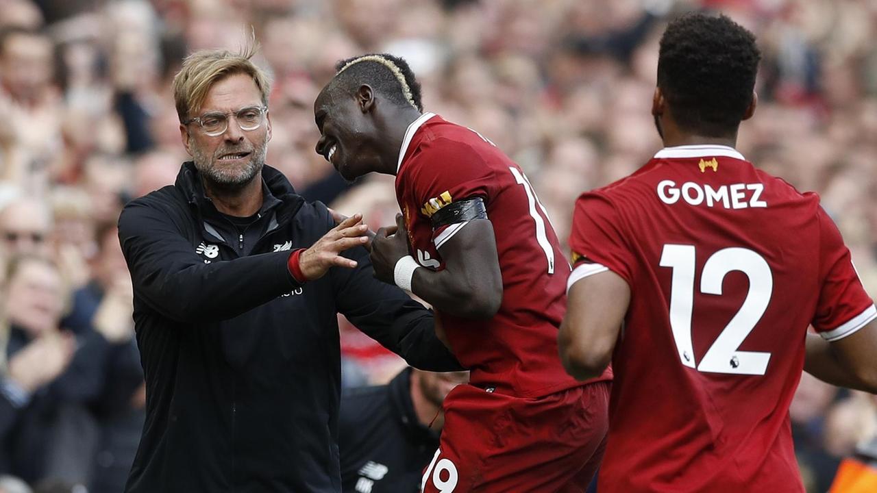 Mane springt Klopp lachend an, im Vordergrund läuft der Spieler Joe Gomez auf die beiden zu. Mane springt Klopp lachend an, im Vordergrund läuft der Spieler Joe Gomez auf die beiden zu.