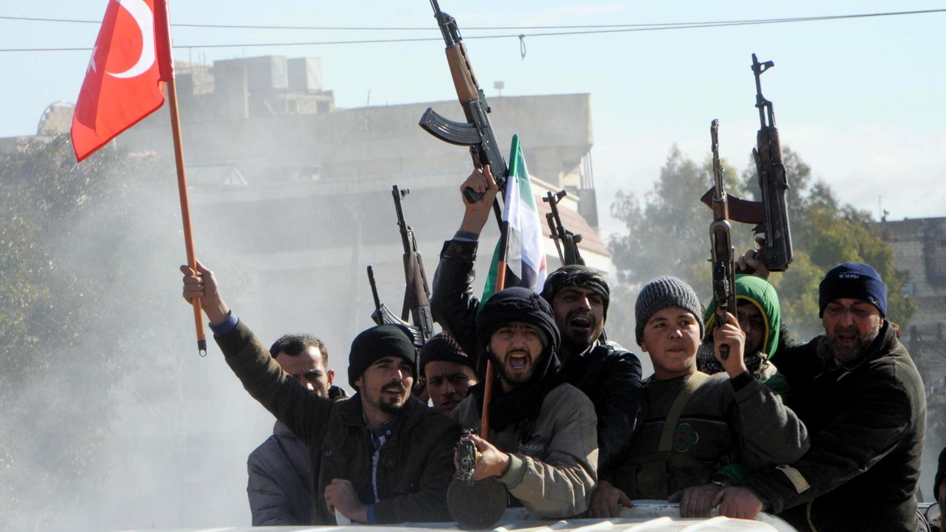 Kämpfer der Freien Syrischen Armee (FSA), die von der Türkei unterstützt werden, fahren mit erhobenen Waffen und einer türkischen Flagge durch die Stadt Azez. Kämpfer der Freien Syrischen Armee (FSA), die von der Türkei unterstützt werden, fahren mit erhobenen Waffen und einer türkischen Flagge durch die Stadt Azez.