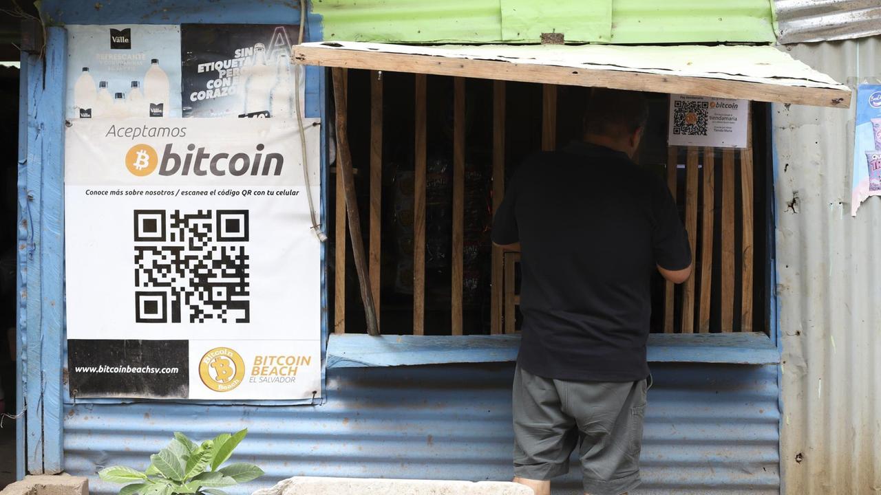 Ein Mann kauft an einem Stand ein, der mit einem Schild dafür wirbt Bitcoin als Zahlungsmittel zu akzeptieren.