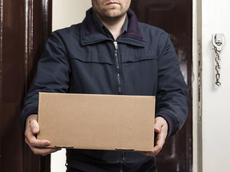Ein Postbote bringt ein Paket an die Haustüre.