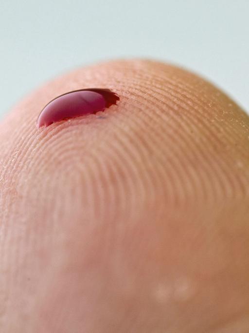 Ein kleiner Blutstropfen auf einem Finger. Mithilfe eines solchen Tropfens und eines Messgerätes können zum Beispiel an Diabetes erkrankte Menschen den Zuckergehalt des Blutes bestimmen.