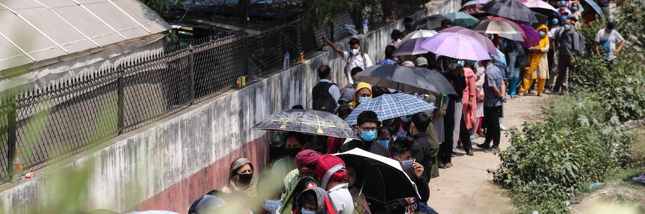 Lange Schlangen vor einem Impfzentrum in Nepals Hauptstadt Kathmandu. Viele Menschen schützen sich mit Regenschirmen vor der Sonne. Lange Schlangen vor einem Impfzentrum in Nepals Hauptstadt Kathmandu. Viele Menschen schützen sich mit Regenschirmen vor der Sonne.