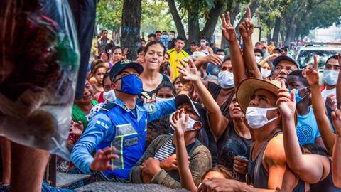Menschen in San Pedro, Honduras, die für Essen einer Hilfsorganisation anstehen. Sie stehen mit Gesichtsmasken dicht gedrängt vor einem Lkw und strecken die Arme aus. 17.04.2020