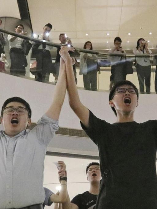 Demonstranten singen in einem Einkaufszentrum und halten sich an den Händen.