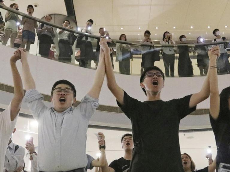 Demonstranten singen in einem Einkaufszentrum und halten sich an den Händen.