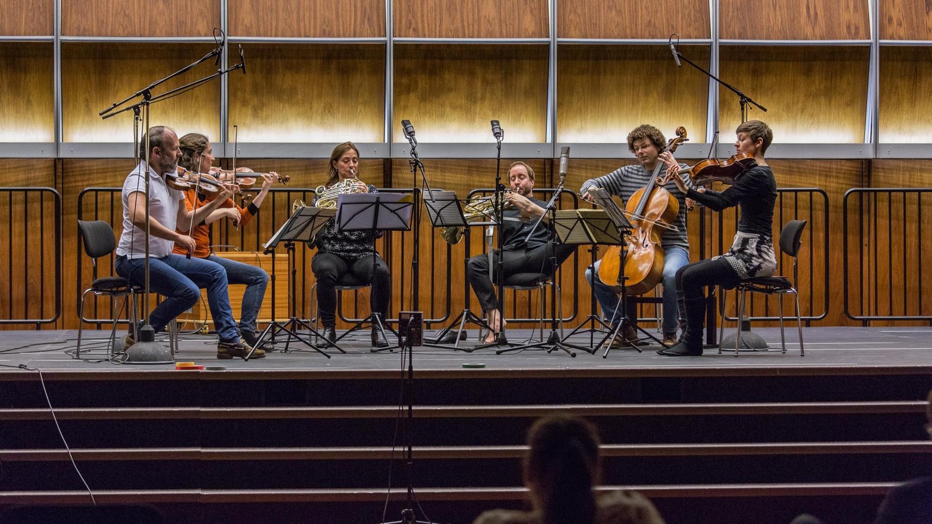 Sechs Musikerinnen und Musiker spielen auf der mit Mikrofonen bestückten Bühne im holzgetäfelten Dlf Kammermusiksaal Sechs Musikerinnen und Musiker spielen auf der mit Mikrofonen bestückten Bühne im holzgetäfelten Dlf Kammermusiksaal