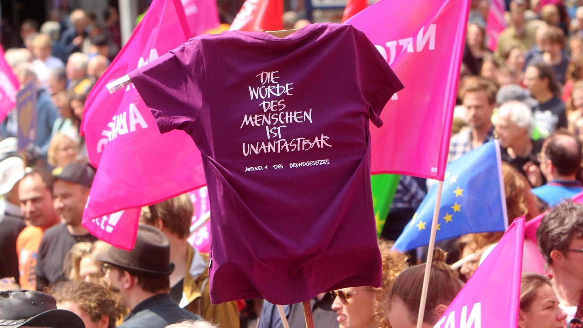 Das Bild zeigt eine Demonstration gegen Nationalismus in Stuttgart, auf der ein T-Shirt mit dem Aufdruck "Die Würde des Menschen ist unantastbar" hochgehalten wird.