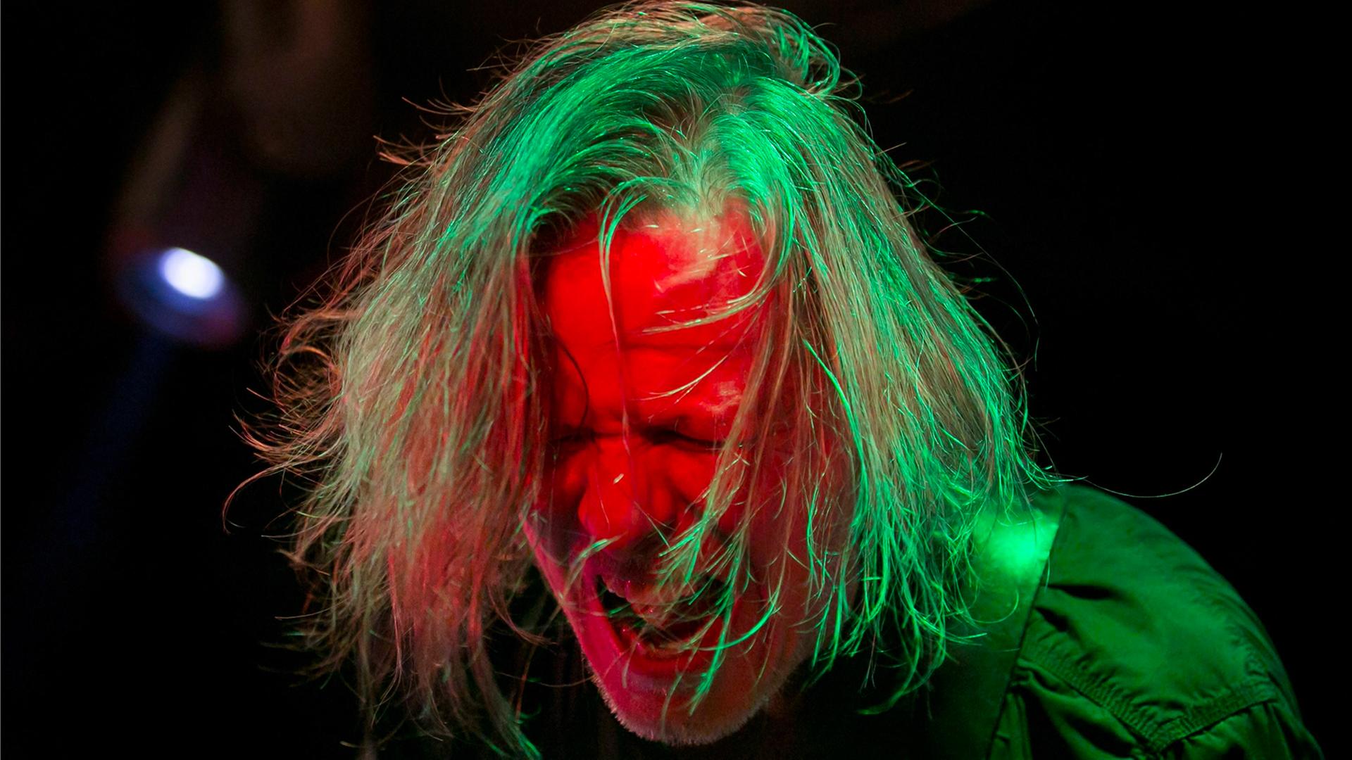 Gitarrist und Sänger Michael Gira der amrerikanischen Post-Punk-Band Swans bei einem Auftritt 2013 im Akvarium Klub in Budapest. Sein Kopf ist grün-rot angestrahlt, das Haar zerzaust, das Gesicht zum Schrei verzerrt. Gitarrist und Sänger Michael Gira der amrerikanischen Post-Punk-Band Swans bei einem Auftritt 2013 im Akvarium Klub in Budapest. Sein Kopf ist grün-rot angestrahlt, das Haar zerzaust, das Gesicht zum Schrei verzerrt.