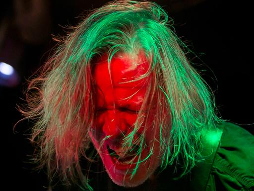 Gitarrist und Sänger Michael Gira der amrerikanischen Post-Punk-Band Swans bei einem Auftritt 2013 im Akvarium Klub in Budapest. Sein Kopf ist grün-rot angestrahlt, das Haar zerzaust, das Gesicht zum Schrei verzerrt.