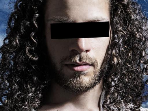 Ein Mann mit langen Haaren hat einen schwarzen Balken vor den Augen, um unkenntlich zu bleiben.