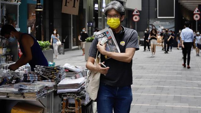 Ein Mann mit einer gelben Mund-Nasen-Maske - ein Symbol der "Regenschirm-Revolution" 2014 - verlässt am 18. Juni 2021 in Hongkong einen Zeitungsverkaufsstand mit einer Ausgabe der "Apple Daily" als Geste der Unterstützung für die Zeitung nach einer Razzia.