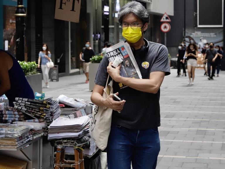 Ein Mann mit einer gelben Mund-Nasen-Maske - ein Symbol der "Regenschirm-Revolution" 2014 - verlässt am 18. Juni 2021 in Hongkong einen Zeitungsverkaufsstand mit einer Ausgabe der "Apple Daily" als Geste der Unterstützung für die Zeitung nach einer Razzia.