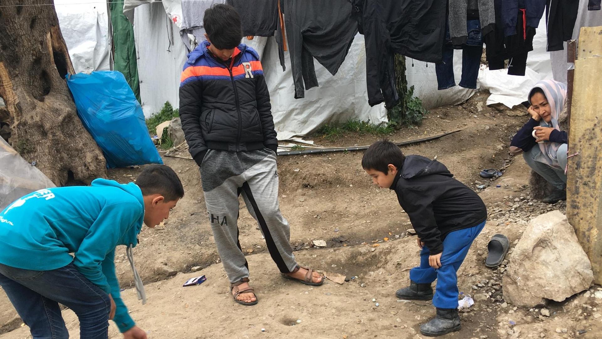 Kinder spielen, in einen sorglosen Moment, mit Murmeln in einem Flüchtlingslager auf Lesbos. Kinder spielen, in einen sorglosen Moment, mit Murmeln in einem Flüchtlingslager auf Lesbos.
