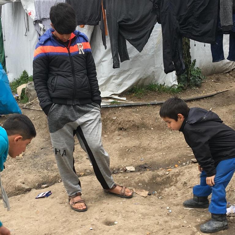 Kinder spielen, in einen sorglosen Moment, mit Murmeln in einem Flüchtlingslager auf Lesbos.