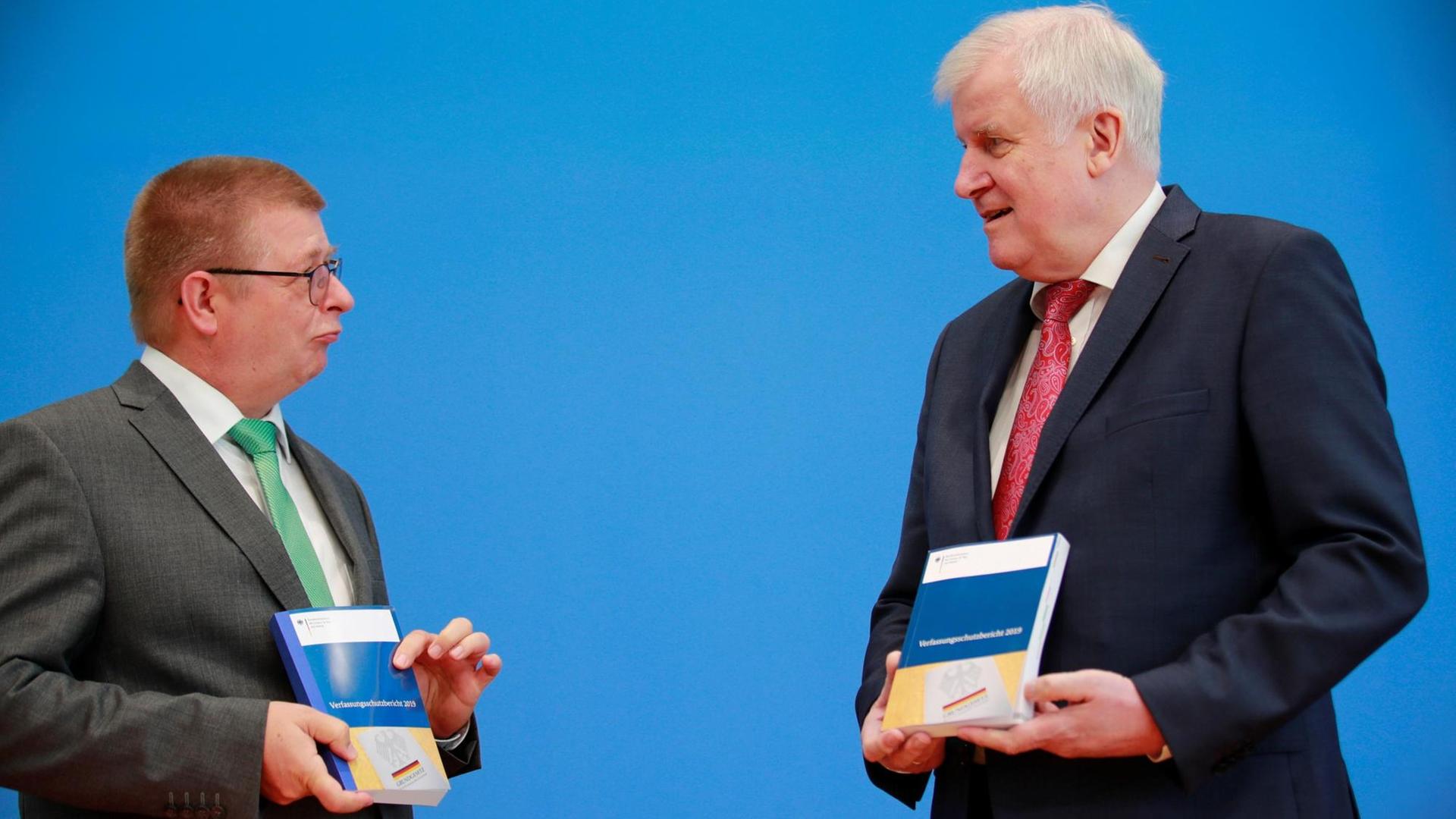 Die beiden stehen sich vor einem blauen Hintergrund gegenüber und reden miteinander. Beide halten den Bericht in den Händen. Die beiden stehen sich vor einem blauen Hintergrund gegenüber und reden miteinander. Beide halten den Bericht in den Händen.