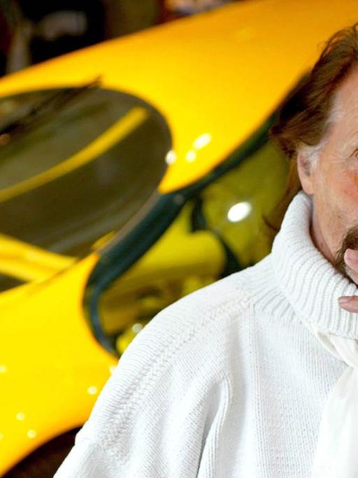 Das Bild zeigt den Designer Luigi Colani mit einer Zigarre im Mund vor einem knallgelben Auto.