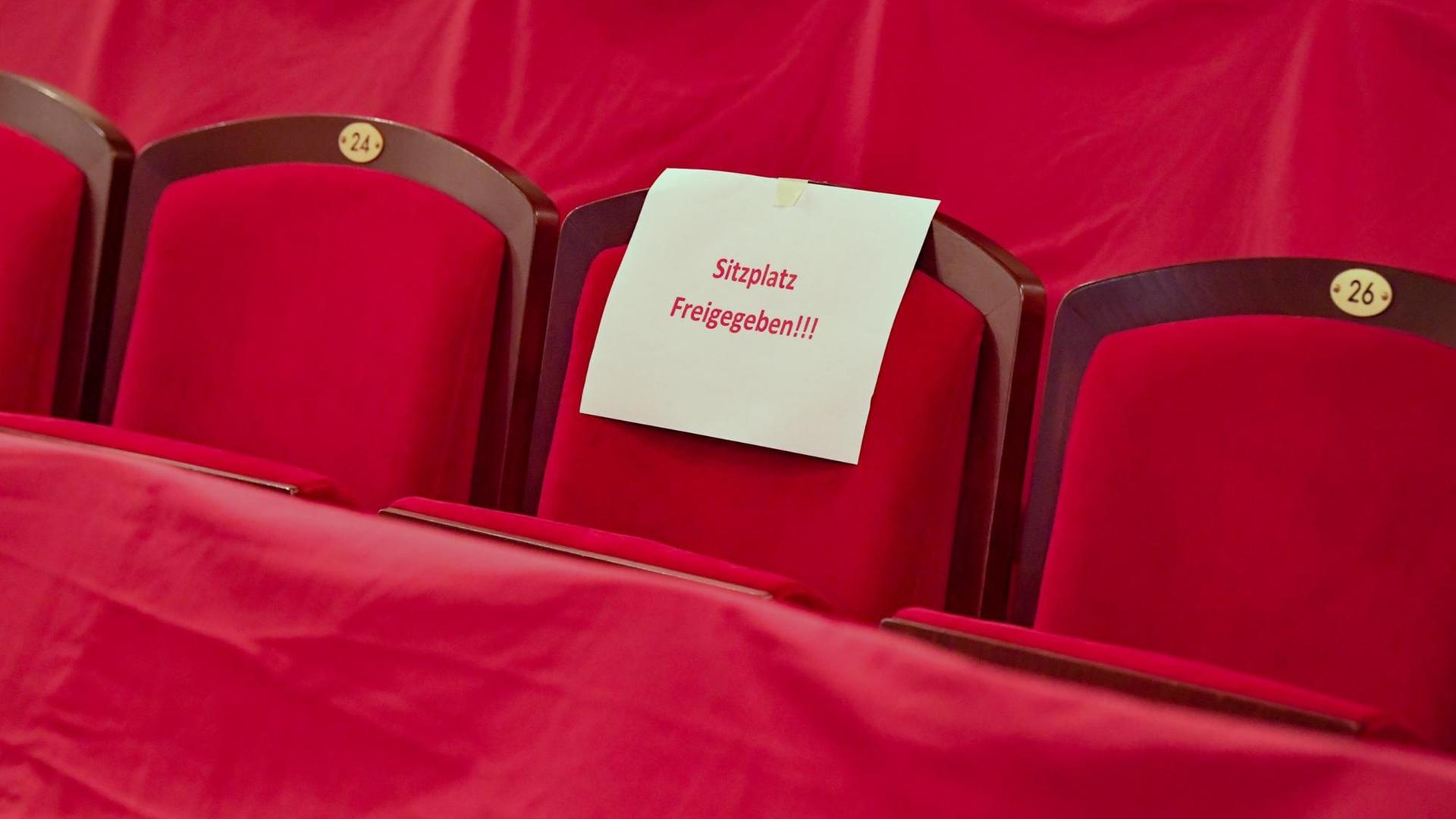 Ein Schild mit der Aufschrift "Sitzplatz freigegeben!!!" liegt auf einem roten Theatersitz.
