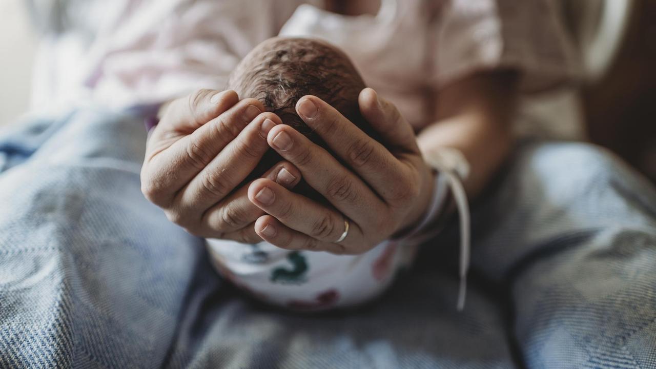 Eine Frau hält den Kopf eines Neugeborenen in ihren Händen. Eine Frau hält den Kopf eines Neugeborenen in ihren Händen.
