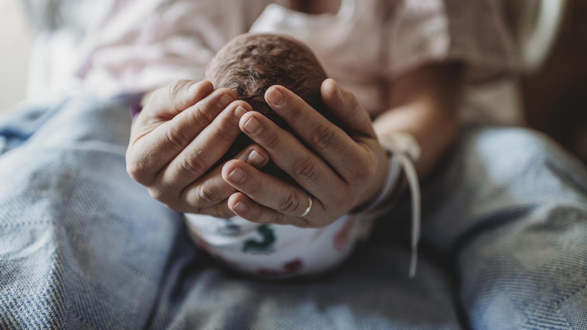 Eine Frau hält den Kopf eines Neugeborenen in ihren Händen. Eine Frau hält den Kopf eines Neugeborenen in ihren Händen.