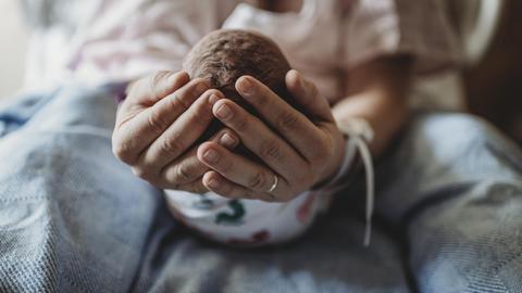 Eine Frau hält den Kopf eines Neugeborenen in ihren Händen.