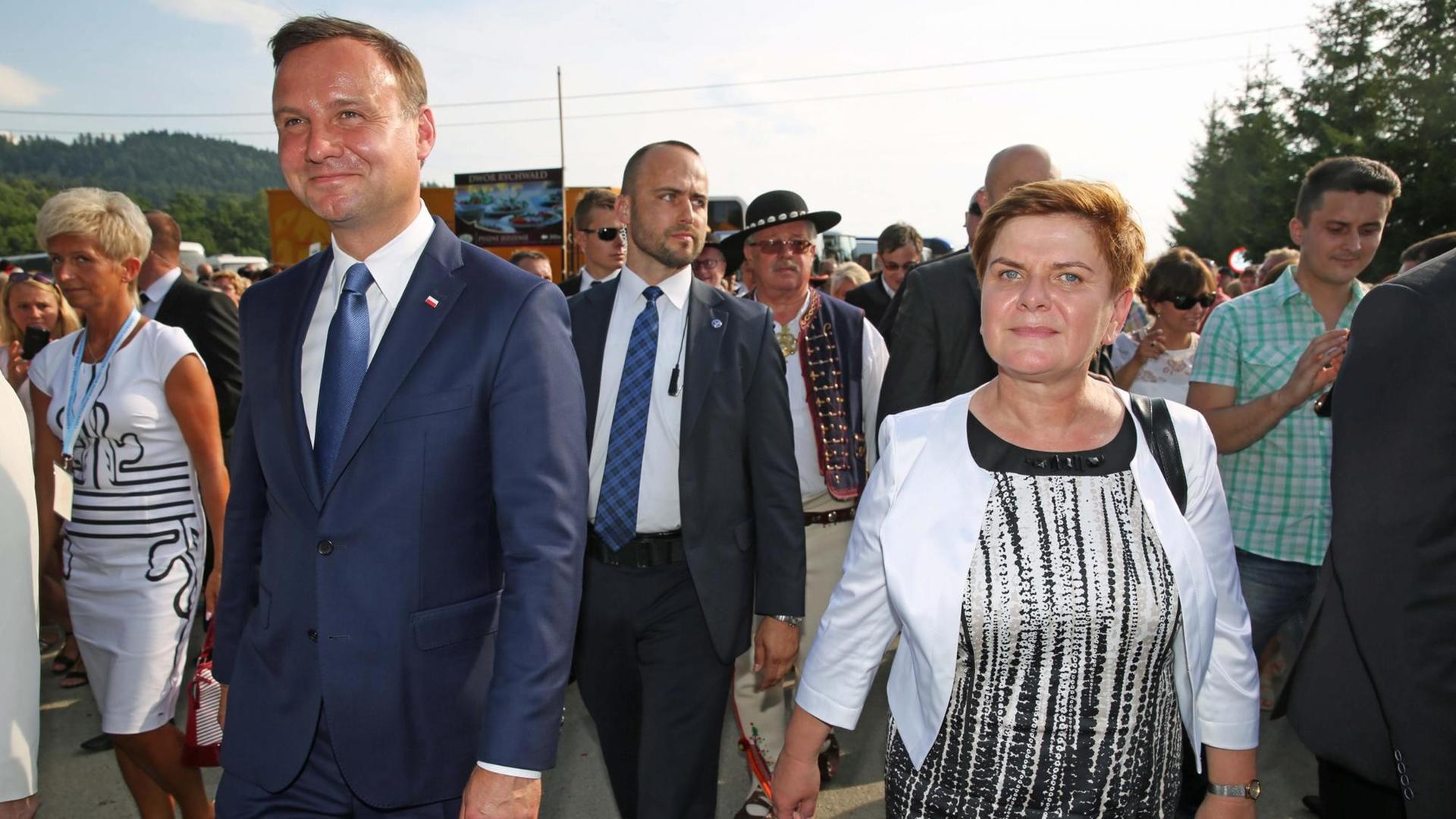 Polens Präsident Andrzej Duda und Spitzenkandidatin Beata Szydlo von der Partei "Recht und Gerechtigkeit" laufen mit anderen Menschen auf einer Straße.