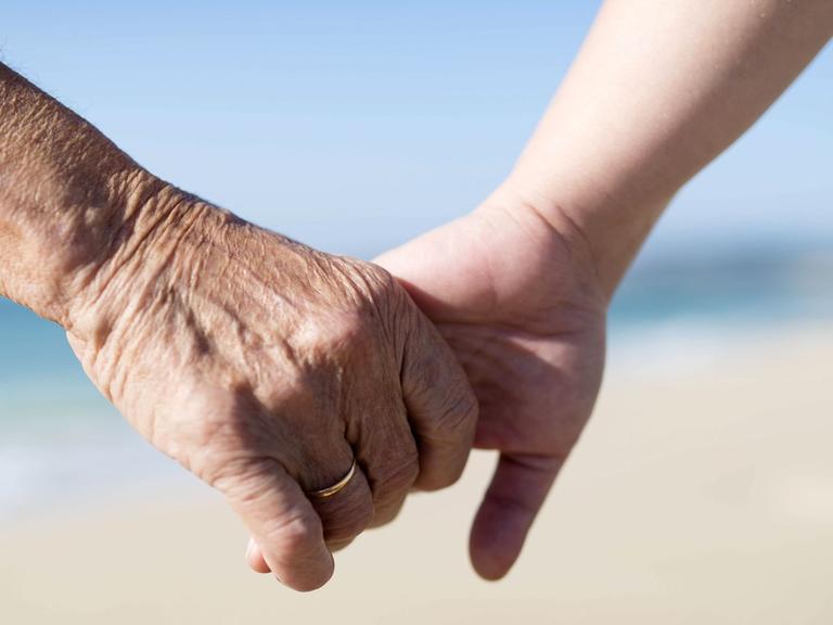 Eine alte und eine junge Frau halten Hände.