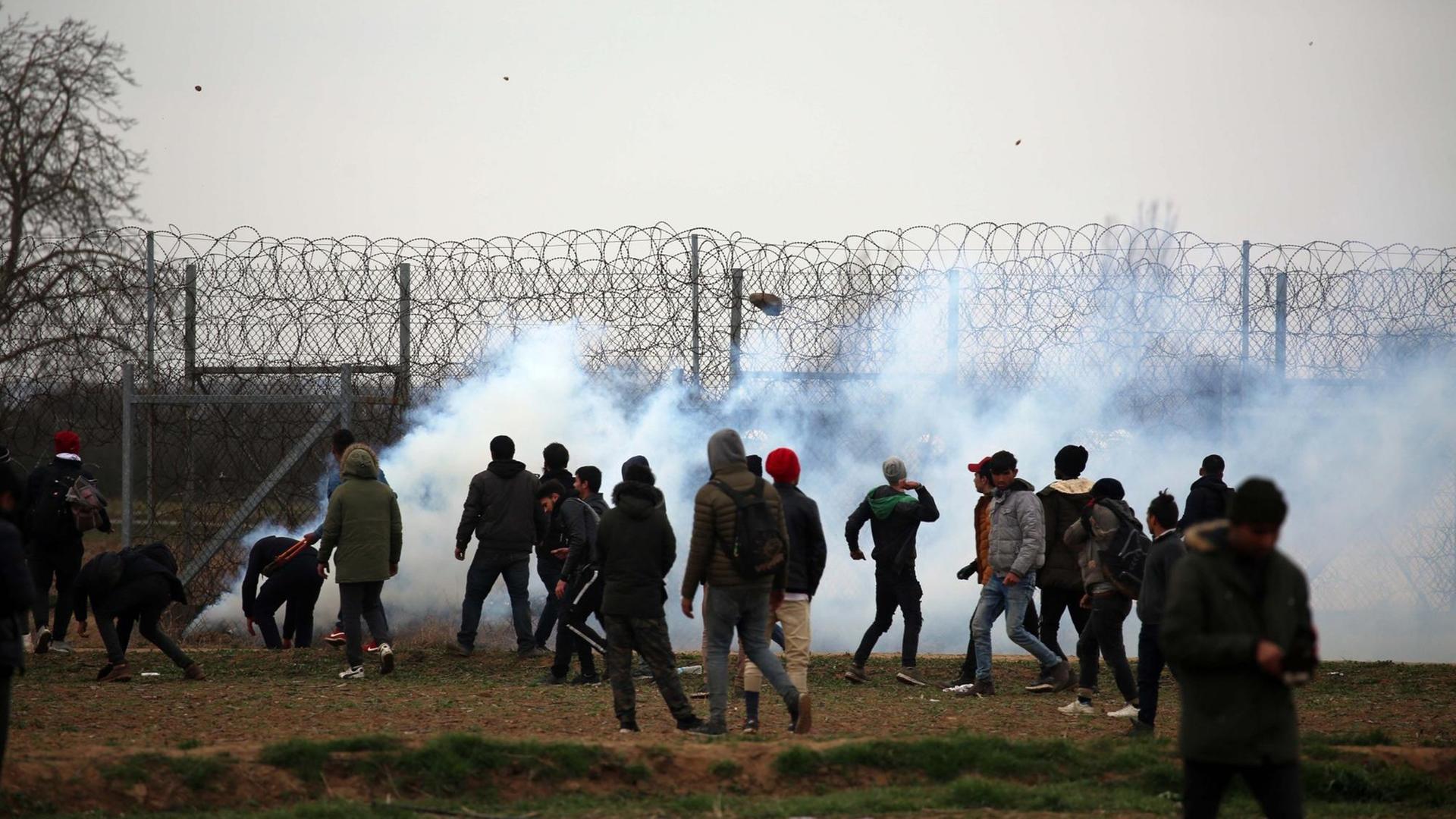 Menschen stehen an der griechisch-türkischen Grenze, an der Tränengas eingesetzt wird Menschen stehen an der griechisch-türkischen Grenze, an der Tränengas eingesetzt wird