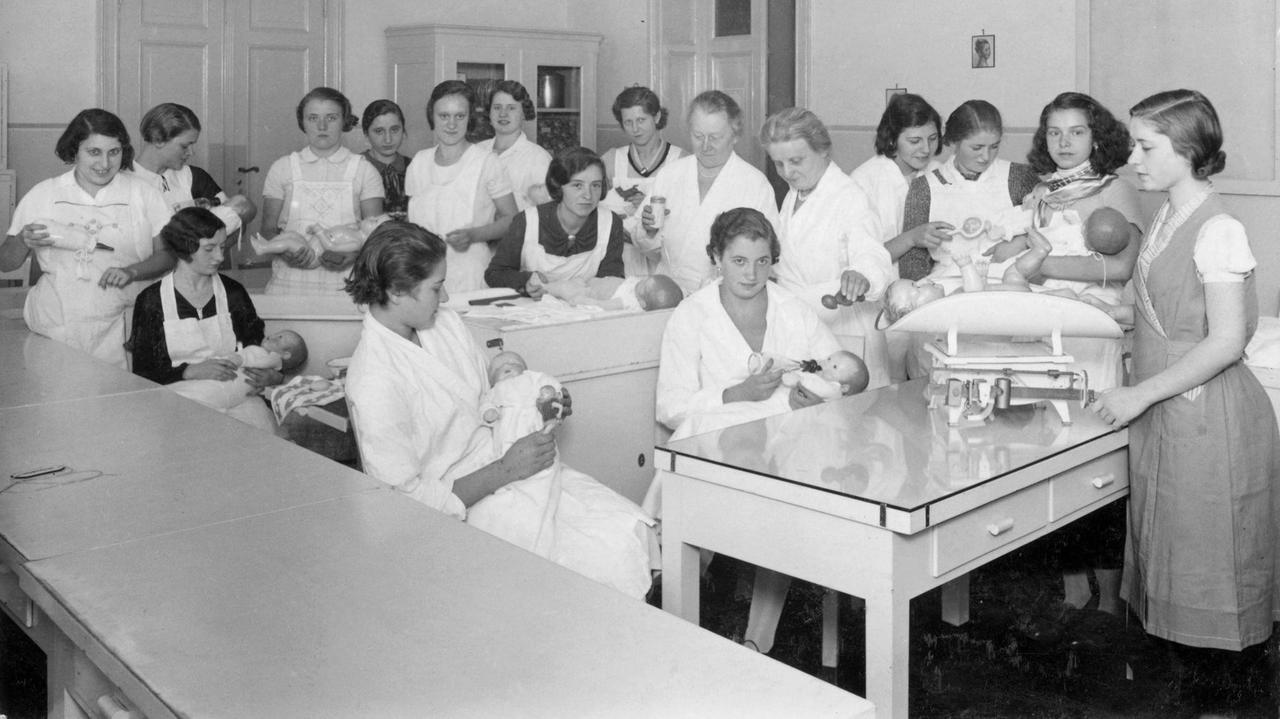 Historisches Foto, vermutlich 1935: Unter Anleitung üben junge Frauen an Babypuppen das Wickeln, Stillen und Füttern Historisches Foto, vermutlich 1935: Unter Anleitung üben junge Frauen an Babypuppen das Wickeln, Stillen und Füttern