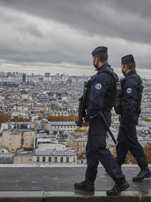Bewaffnete Polizisten mit Masken laufen Patrouille auf dem Vorplatz der Pariser Basilika Sacré Cœur, im Hintergrund eine Aussicht auf die Dächer von Paris.