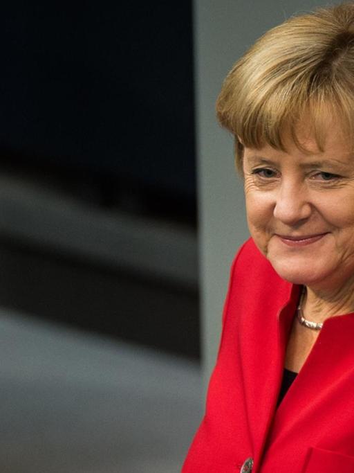 Merkel steht lächelnd im roten Kostüm am Rednerpult.