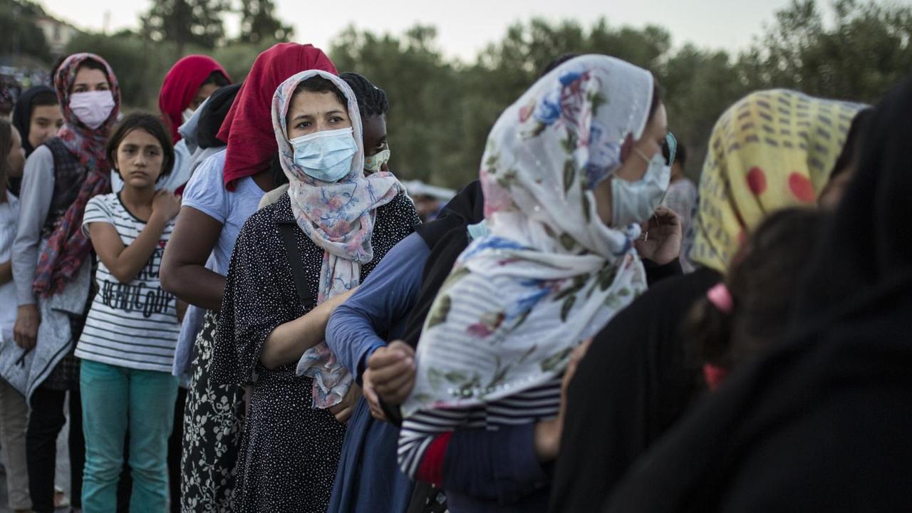 10.09.2020, Griechenland, Moria: Frauen stehen an, um Essen zu erhalten in der Nähe des ausgebrannten Flüchtlingslagers Moria. Mehrere Brände haben das Lager fast vollständig zerstört. 10.09.2020, Griechenland, Moria: Frauen stehen an, um Essen zu erhalten in der Nähe des ausgebrannten Flüchtlingslagers Moria. Mehrere Brände haben das Lager fast vollständig zerstört.