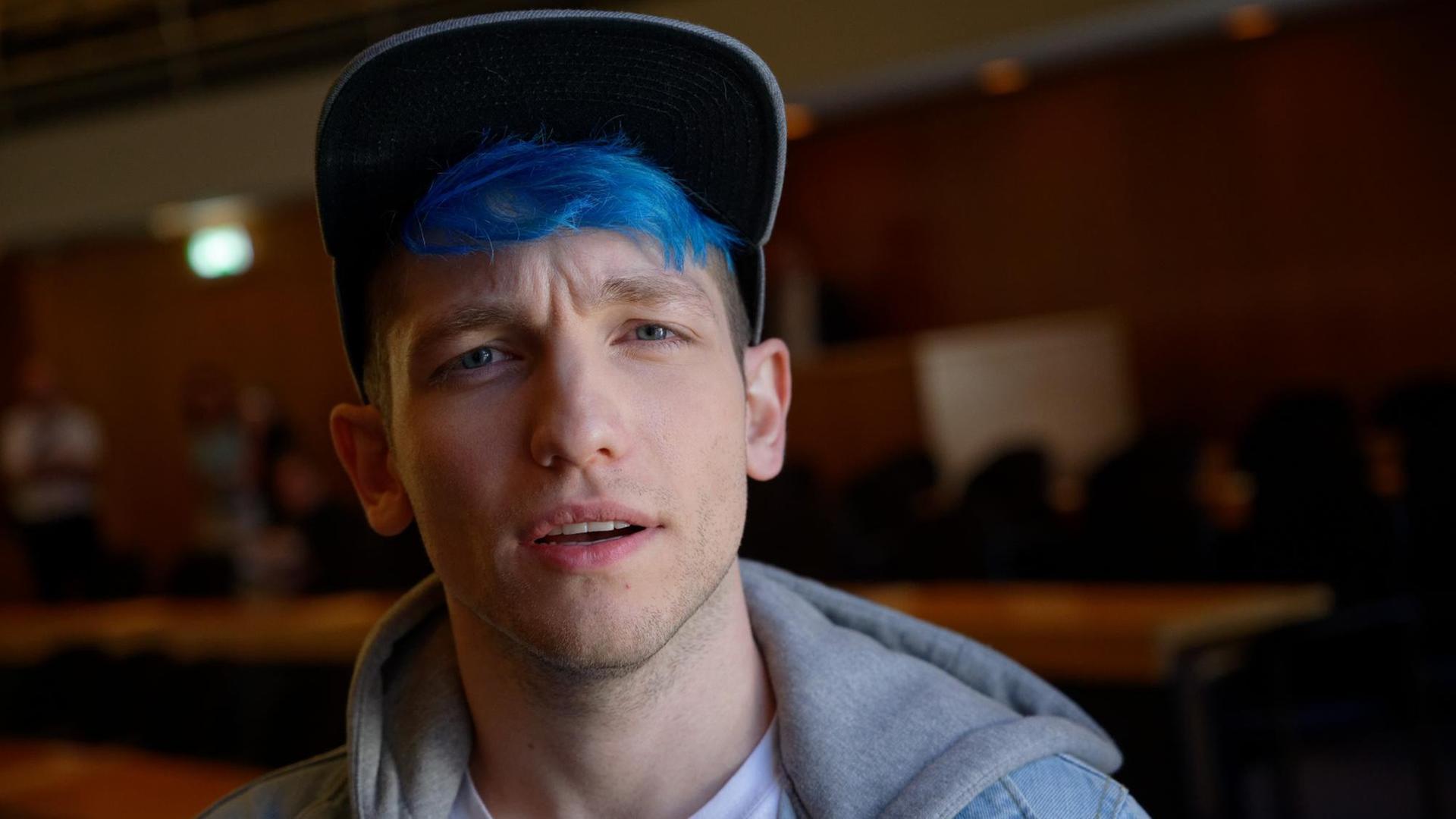 Youtuber Rezo, mit blau gefärbtem Haar und Basecap, schaut skeptisch in die Kamera, im Hintergrund: ein holzgetäfelter Veranstaltungssaal Youtuber Rezo, mit blau gefärbtem Haar und Basecap, schaut skeptisch in die Kamera, im Hintergrund: ein holzgetäfelter Veranstaltungssaal