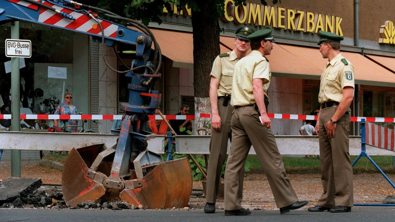 Polizeibeamte sichern vor 25 Jahren eine Baustelle vor der Commerzbankfiliale im Stadtbezirk Zehlendorf. Dort wurde der 70 Meter lange Tunnel freigelegt, durch den im Juni 1995 vier Geiselgangster mit einer Millionenbeute geflüchtet waren. Polizeibeamte sichern vor 25 Jahren eine Baustelle vor der Commerzbankfiliale im Stadtbezirk Zehlendorf. Dort wurde der 70 Meter lange Tunnel freigelegt, durch den im Juni 1995 vier Geiselgangster mit einer Millionenbeute geflüchtet waren.