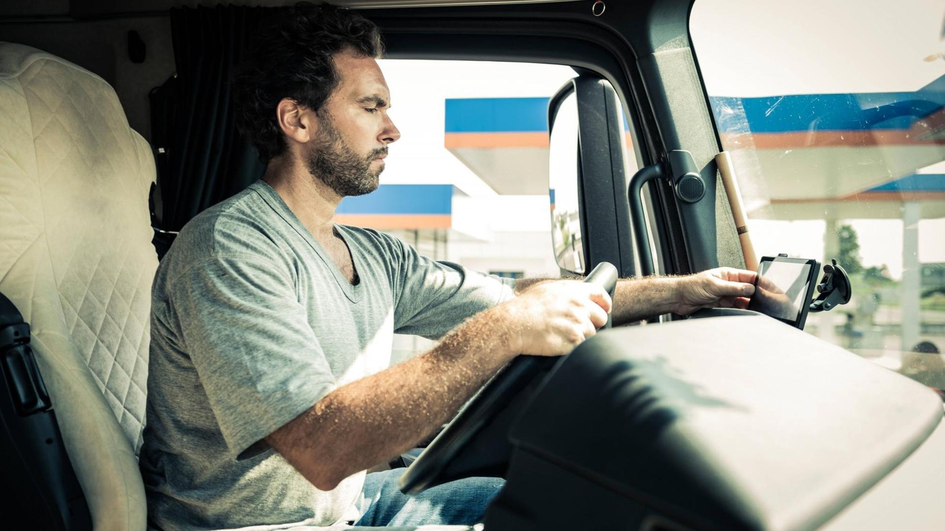 Ein LKW-Fahrer sitzt am Steuer und stellt sein Navigationsgerät ein.