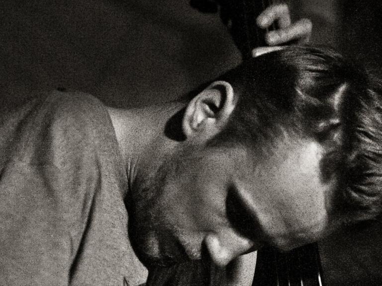 Der Bassist ist auf einem s/w Bild vertieft in sein Spiel zu sehen