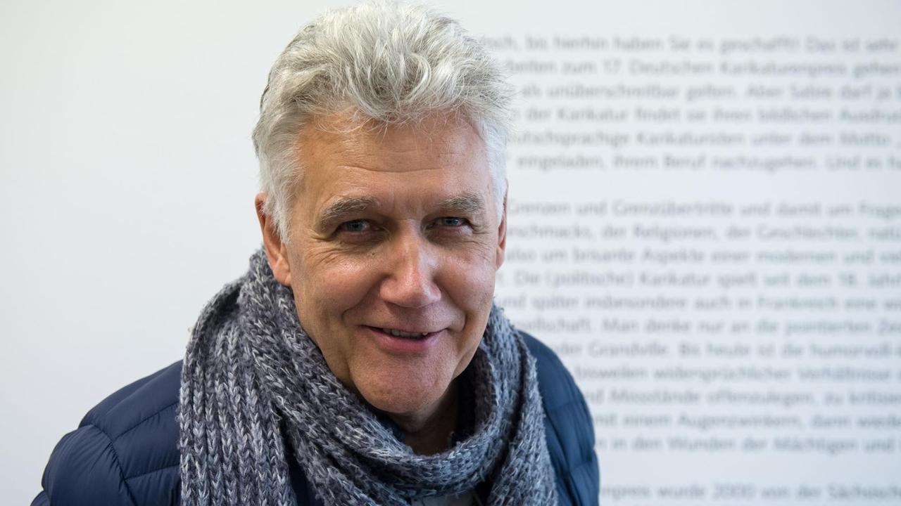 Ein älterer Mann mit grauem Haar und Wollschal lächelt in die Kamera. Ein älterer Mann mit grauem Haar und Wollschal lächelt in die Kamera.