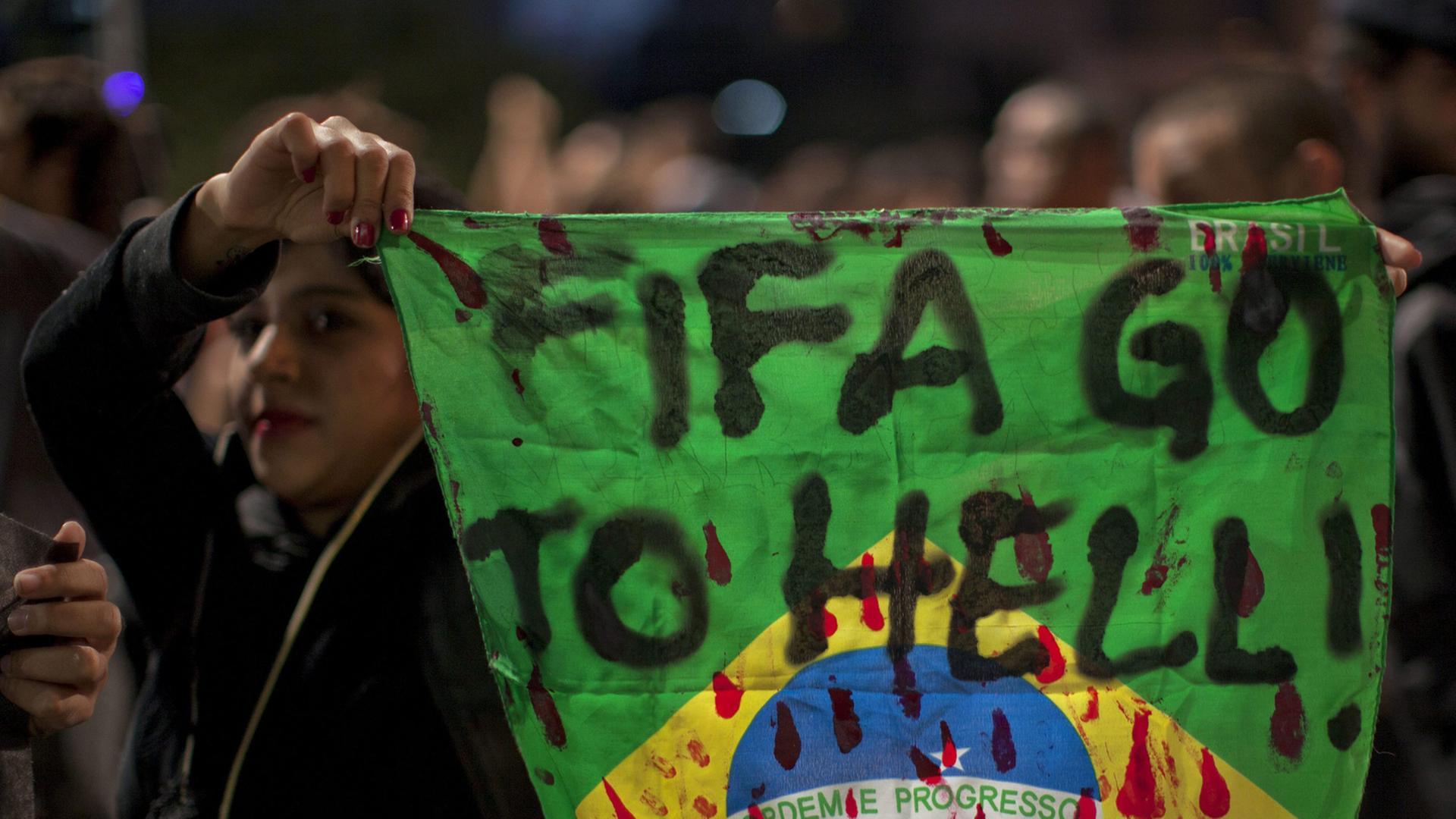 Eine Demonstrantin hält in Sao Paula eine Fahne Brasiliens mit der Aufschrift "Fifa, fahre zur Hölle!" in die Höhe. Eine Demonstrantin hält in Sao Paula eine Fahne Brasiliens mit der Aufschrift "Fifa, fahre zur Hölle!" in die Höhe.