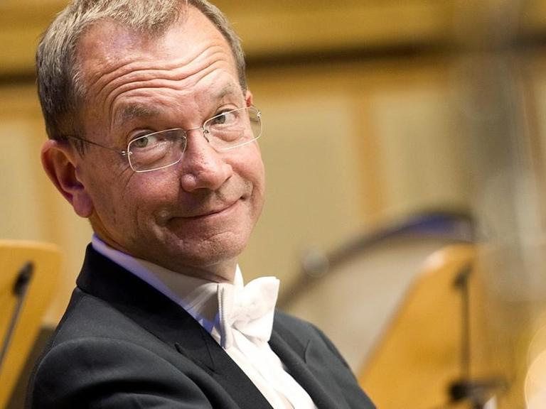Mann im Frack sitzt mit Horn im Orchester