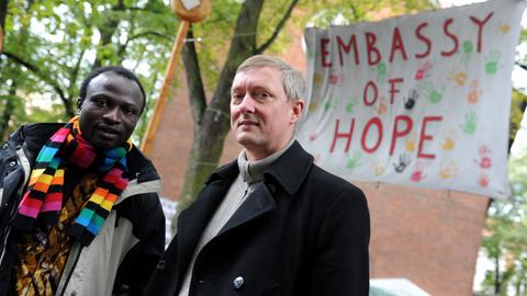 Andreas (links), einer der afrikanischen Flüchtlinge, die in der St.-Pauli-Kirche Unterschlupf gefunden haben, und der Pastor Sieghard Wilm vor der Hamburger St.-Pauli-Kirche; Aufnahme vom Oktober 2013