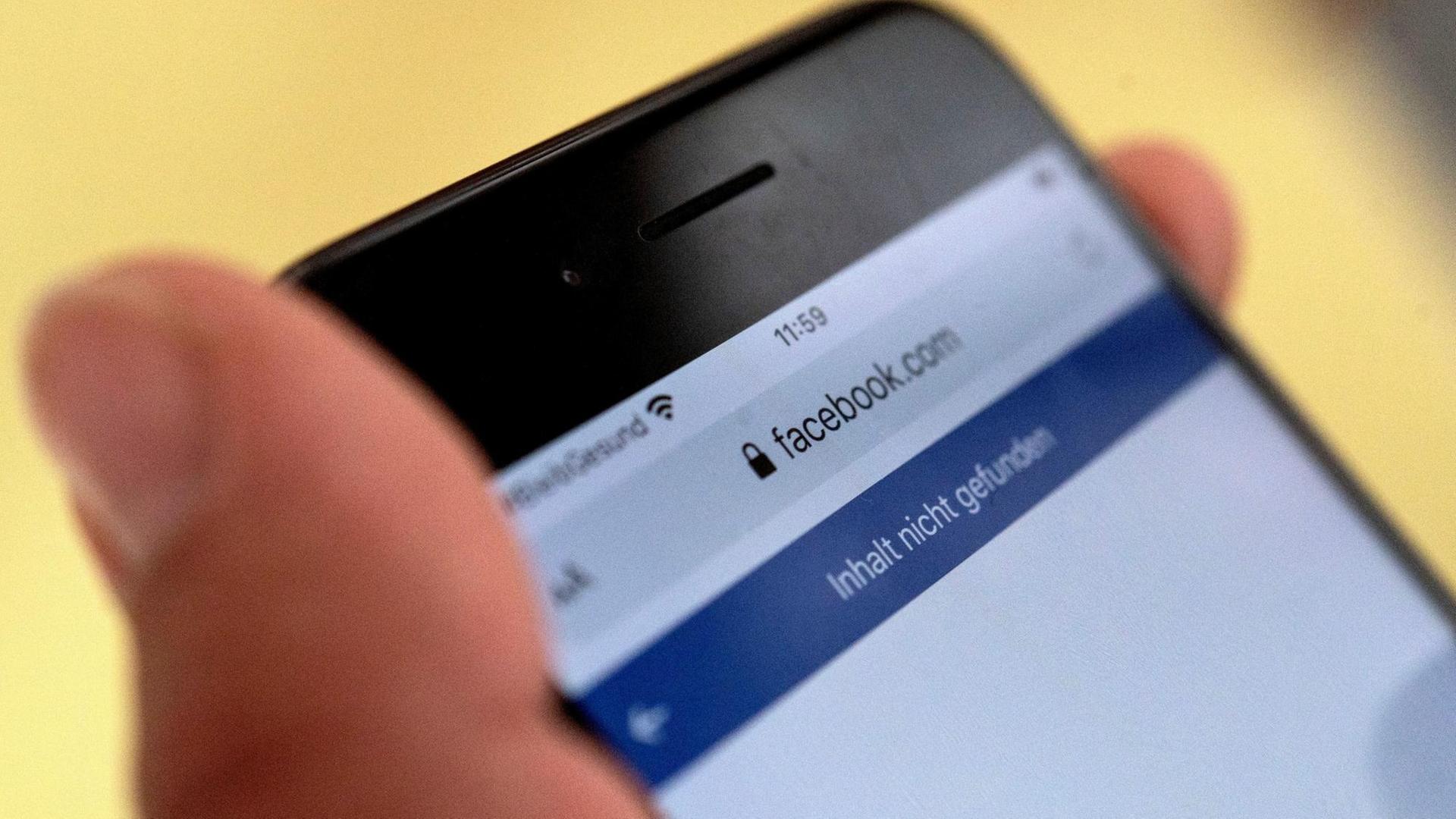 Eine Hand, die ein Smartphone hält, auf dem Facebook zu sehen ist. Eine Hand, die ein Smartphone hält, auf dem Facebook zu sehen ist.