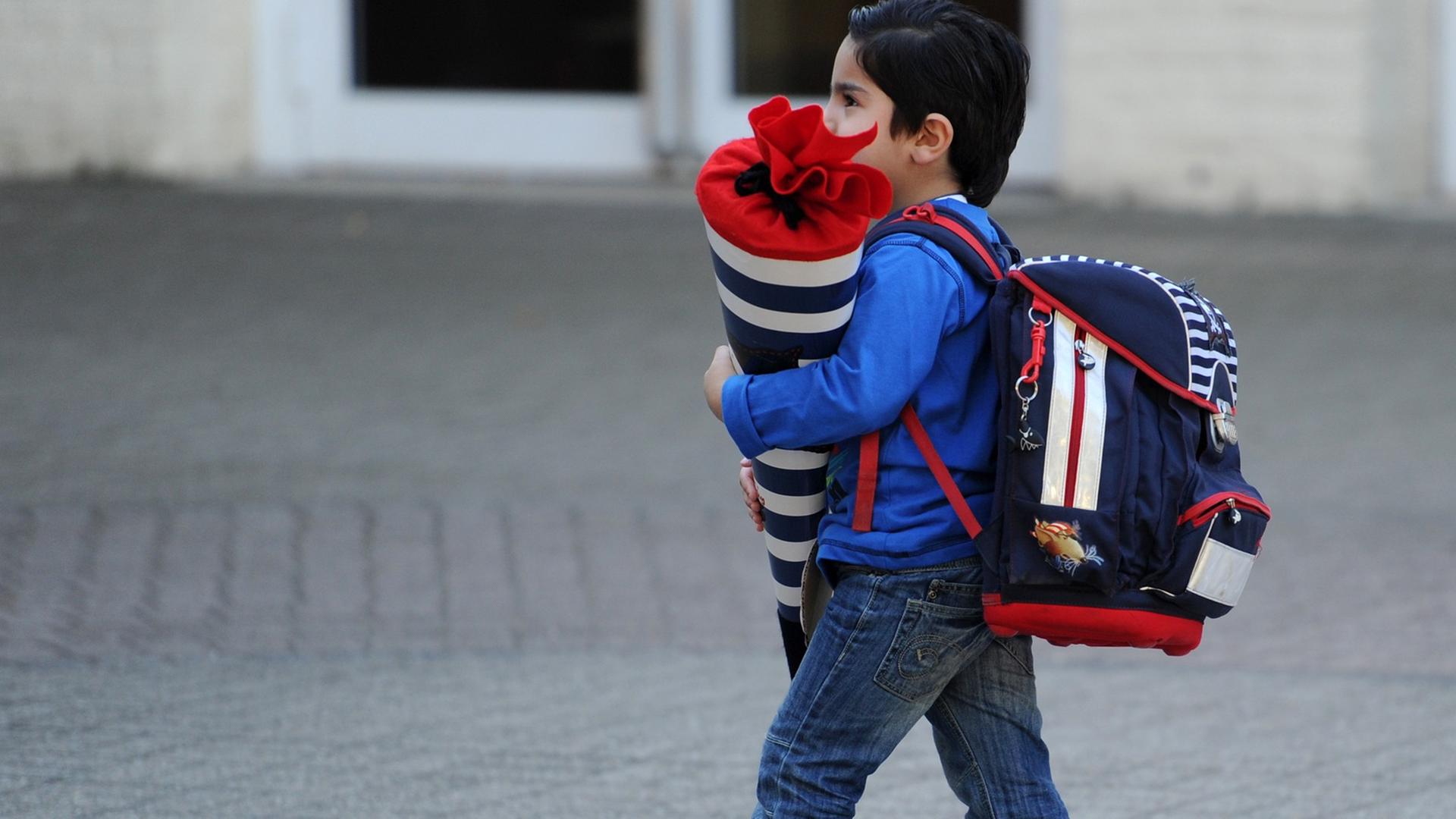 Ein Junge mit Schultüte auf dem Arm und Rucksack auf dem Rücken auf dem Weg zu seiner Einschulung.