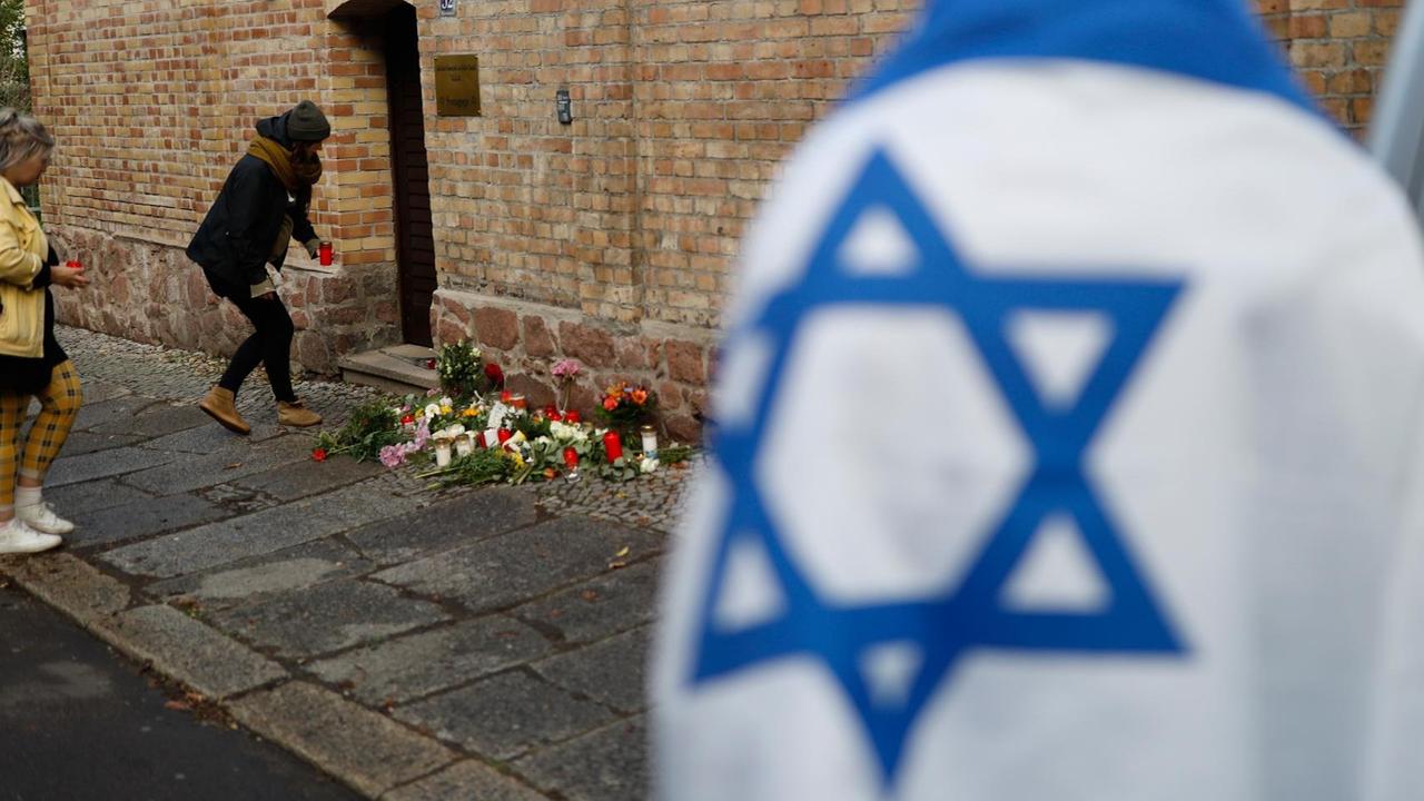 Menschen legen Blumen nieder an der Mauer des jüdischen Friedhofs in Halle (Saale)