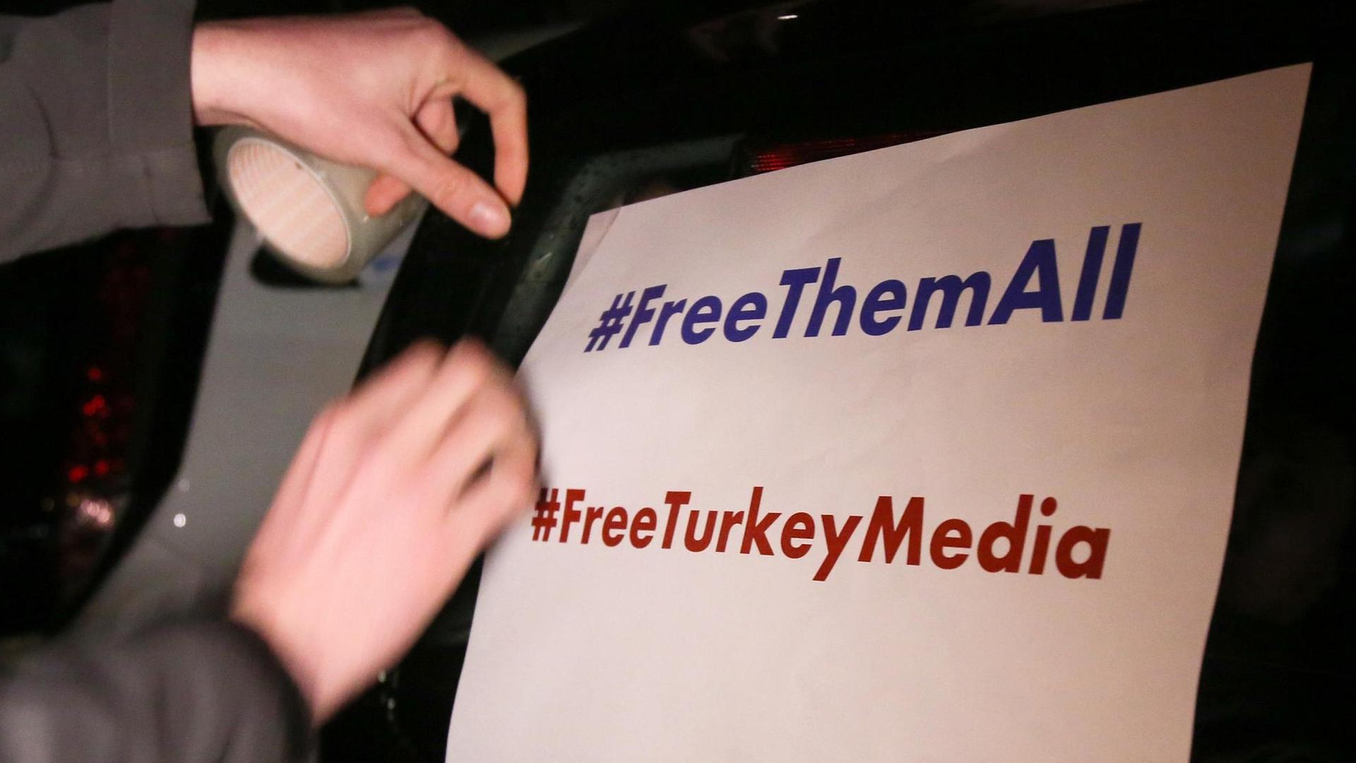 Ein Mann klebt ein Plakat mit der Aufschrift "#FreeThemAll" und "FreeTurkeyMedia" vor dem Start eines Autokorsos für den "Welt"-Korrespondenten Deniz Yücel an einen Pkw. Ein Mann klebt ein Plakat mit der Aufschrift "#FreeThemAll" und "FreeTurkeyMedia" vor dem Start eines Autokorsos für den "Welt"-Korrespondenten Deniz Yücel an einen Pkw.