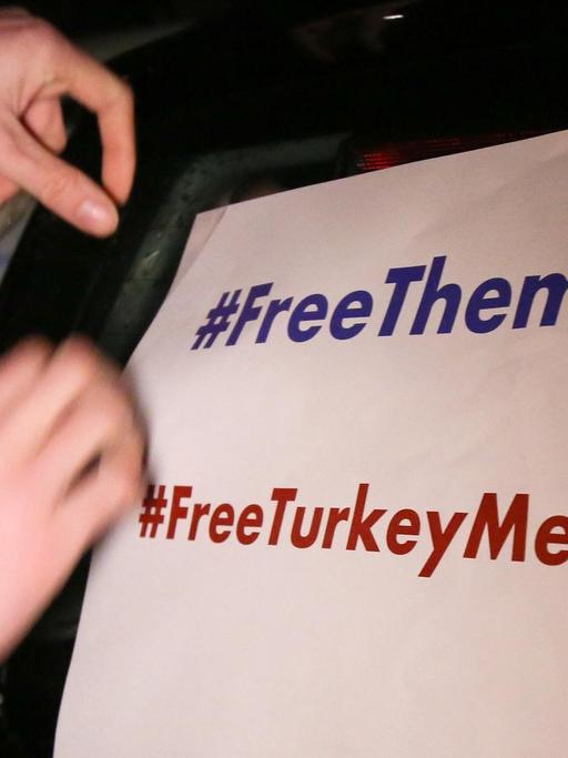 Ein Mann klebt ein Plakat mit der Aufschrift "#FreeThemAll" und "FreeTurkeyMedia" vor dem Start eines Autokorsos für den "Welt"-Korrespondenten Deniz Yücel an einen Pkw.