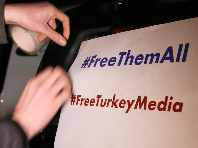 Ein Mann klebt ein Plakat mit der Aufschrift "#FreeThemAll" und "FreeTurkeyMedia" vor dem Start eines Autokorsos für den "Welt"-Korrespondenten Deniz Yücel an einen Pkw.