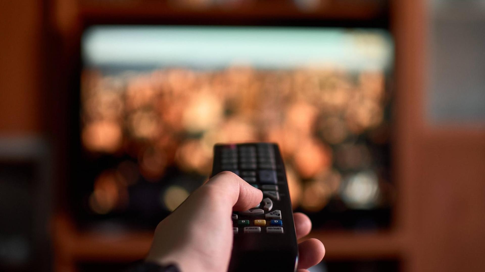 Eine Hand hält eine Fernbedienung und richtet sie auf einen Fernseher, Symbolfoto Eine Hand hält eine Fernbedienung und richtet sie auf einen Fernseher, Symbolfoto