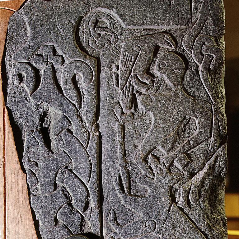 Das Relief des Andreas-Steins zeigt eine Szene der Ragnarök-Sage vom Untergang der Götter: Der Gott Odin wird vom Wolf Fenir gefressen, ein Rabe sitzt auf seiner Schulter. Das Relief wurde ca. 1000 v. Chr. von Wikingern gefertigt und stammt von der Isle of Man, England.